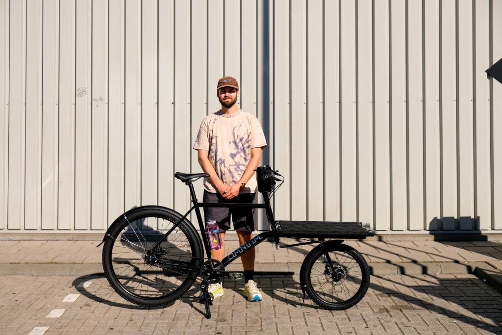 Rokus - Owner of Studio Rook, bicycle (re)building space,  in front of a Omnium Bike